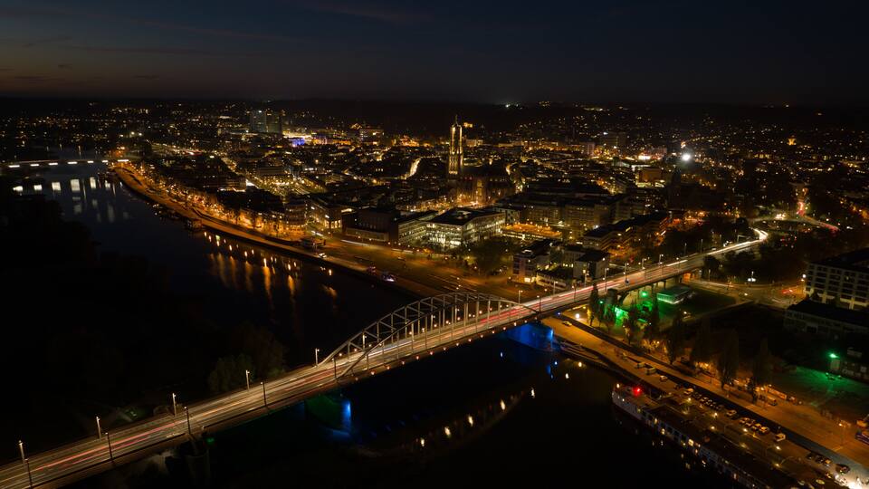 A nighttime cityscape with a prominent bridge, illuminated buildings, and a river reflecting city lights.