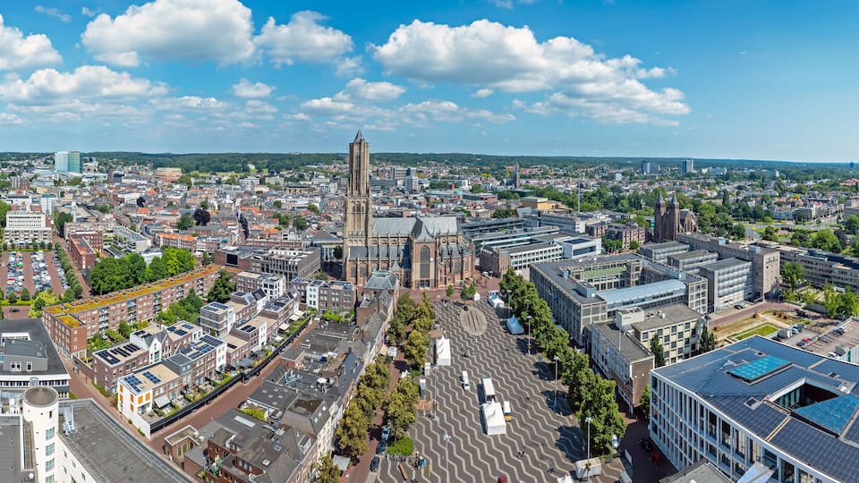 An aerial view of a city with a prominent church tower, a river, and surrounding urban buildings.