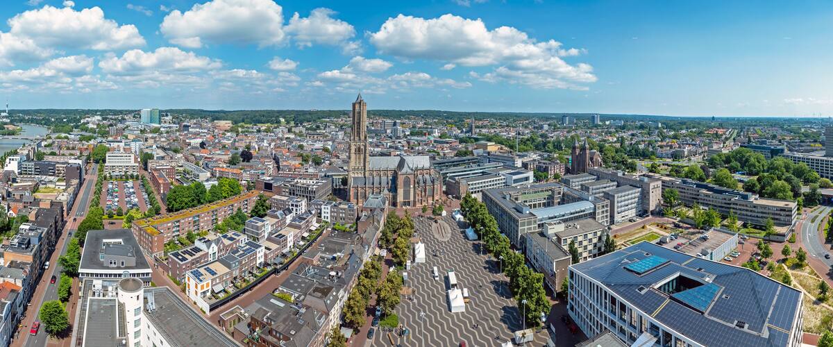 An aerial view of a city with a prominent church tower, a river, and surrounding urban buildings.
