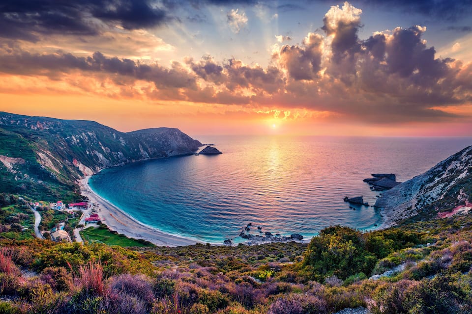 A coastal landscape with a winding road, a beach, and rocky cliffs.