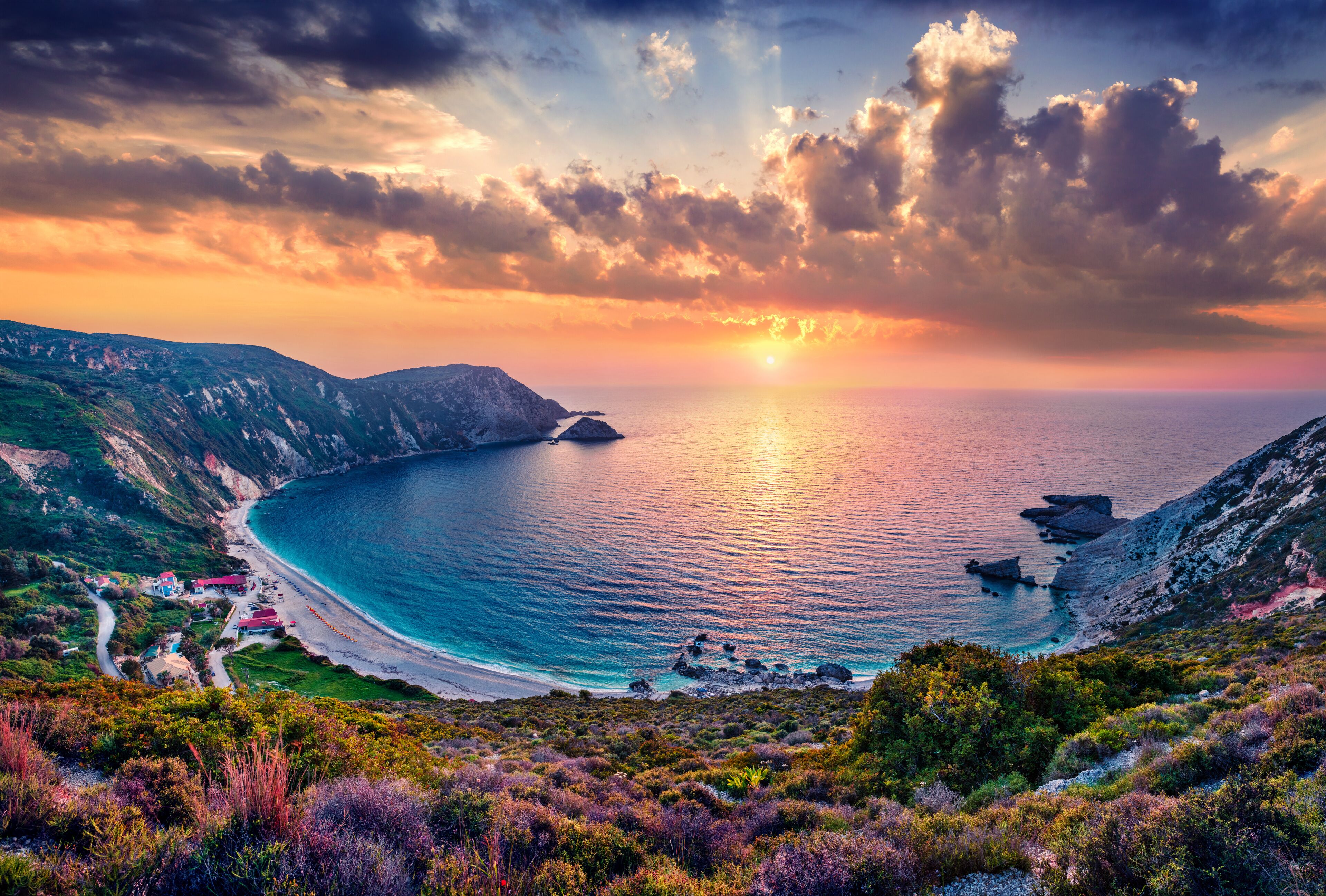 A coastal landscape with a winding road, a beach, and rocky cliffs.