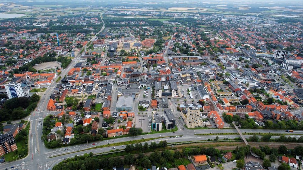 Une vue aérienne d’une ville avec des bâtiments aux toits rouges, une rivière et une autoroute.