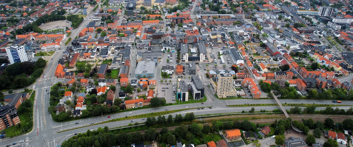 An aerial view of a city with red-roofed buildings, a river, and a highway.