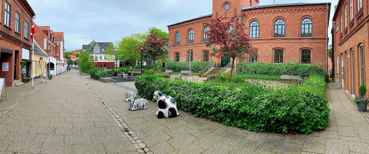 A cobblestone street lined with historic red brick buildings, a small park with benches, and a zebra statue.