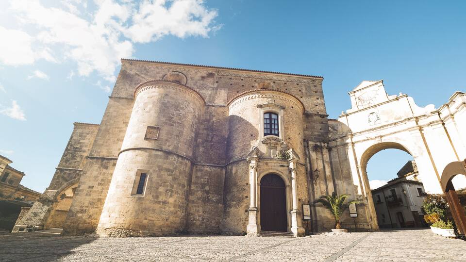 A historic stone building with a large arched entrance, a round tower, and a smaller window.