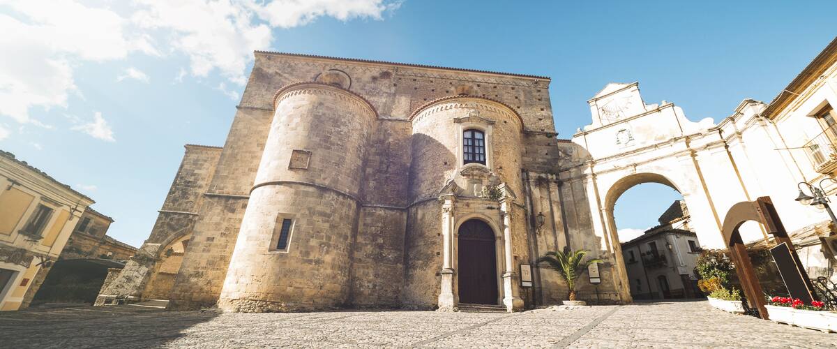 A historic stone building with a large arched entrance, a round tower, and a smaller window.