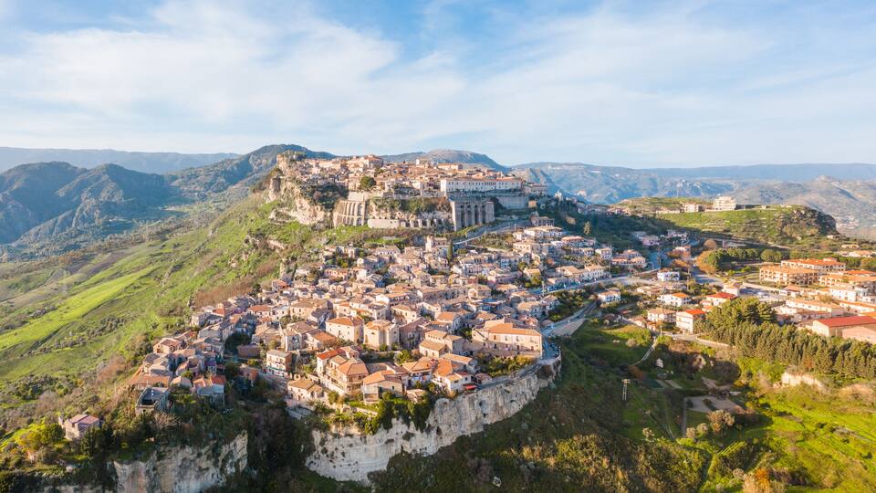 A town perched on a cliff with a historic church and buildings overlooking a valley.