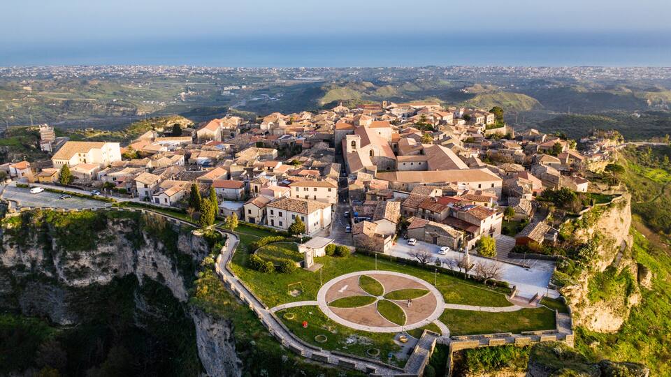 A coastal town with historic buildings, a fortified wall, and a cliff overlooking the sea.