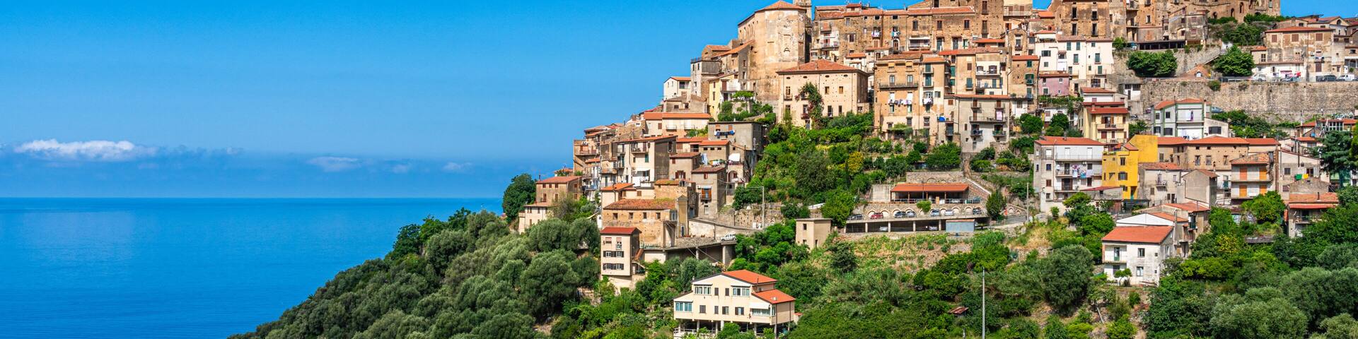 A coastal town with terraced buildings, dense greenery, and a clear blue sea.