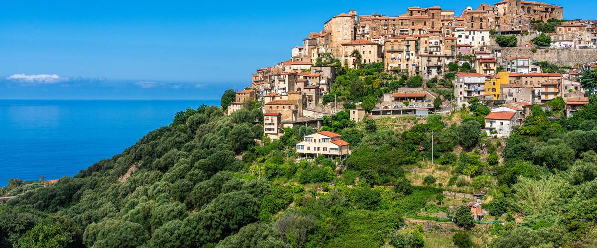 A coastal town with terraced buildings, dense greenery, and a clear blue sea.