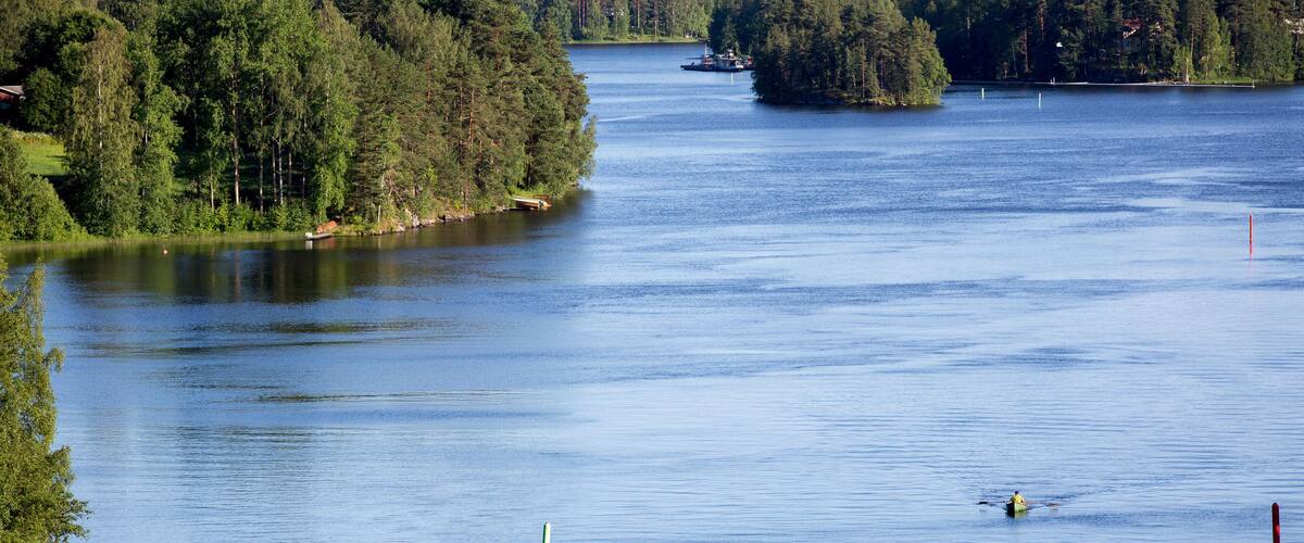 A calm lake surrounded by dense forest and a small boat on the water.