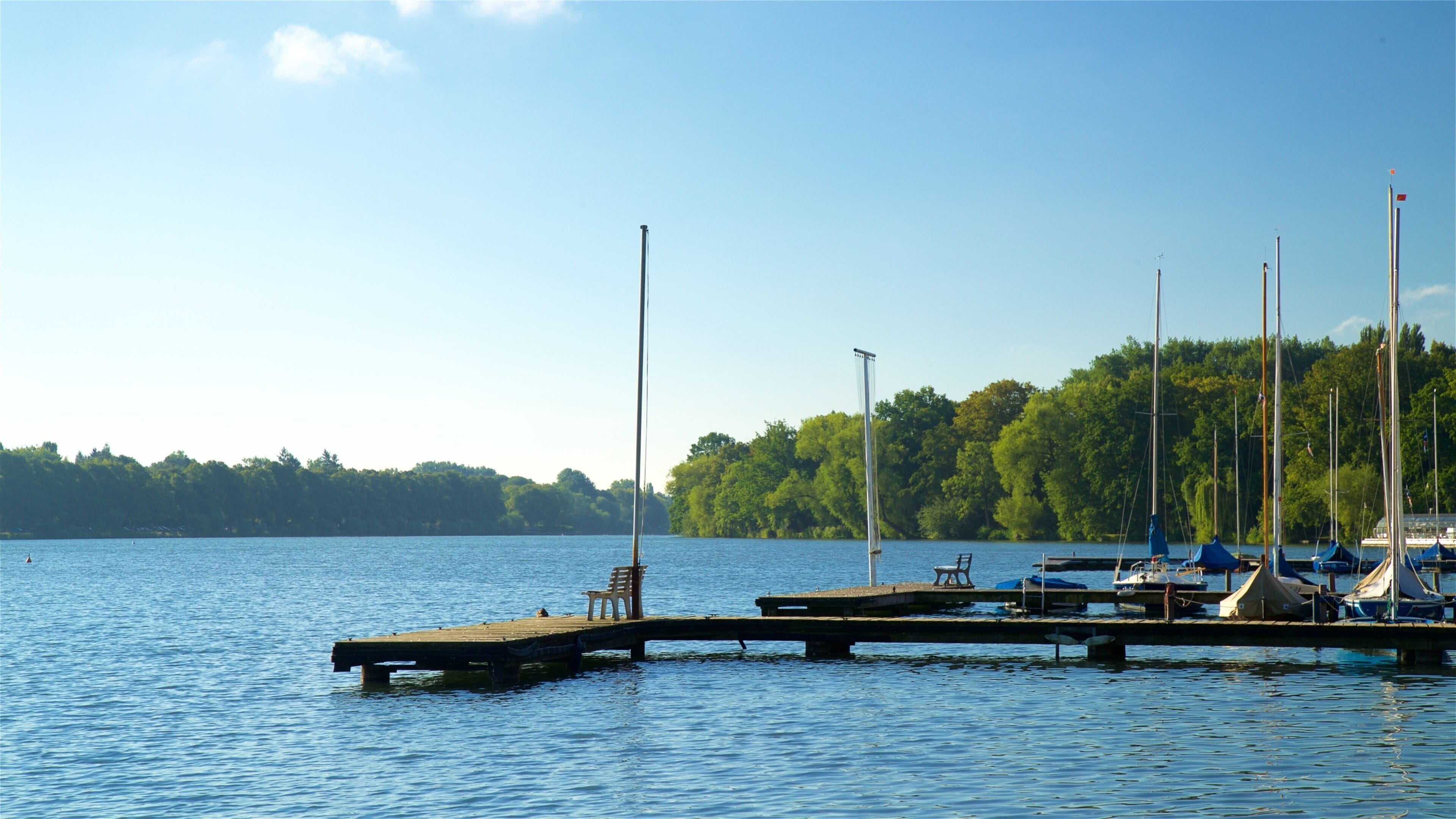 Ein ruhiger See mit einem hölzernen Steg und mehreren Segelbooten, die in der Nähe des Ufers ankern.