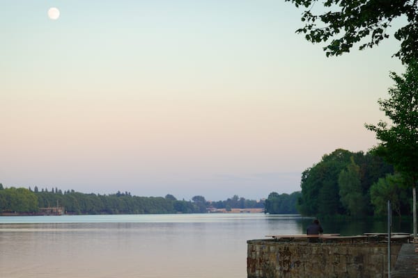 Un lac paisible, avec une jetée en bois et des tables de pique-nique, entouré d’arbres et bordé par une rive éloignée.