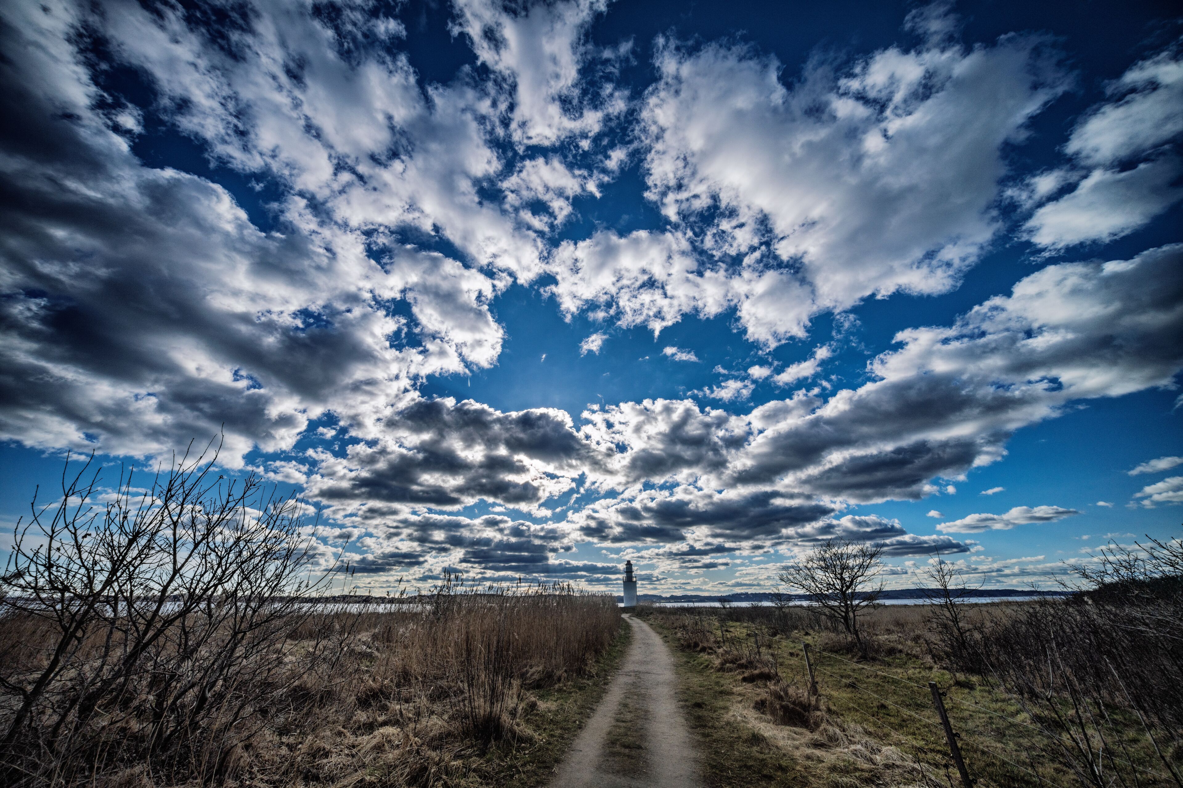 Scenic Coastal Lighthouse Amid Grassy Path Under a Dramatic Cloudy Sky, Denmark