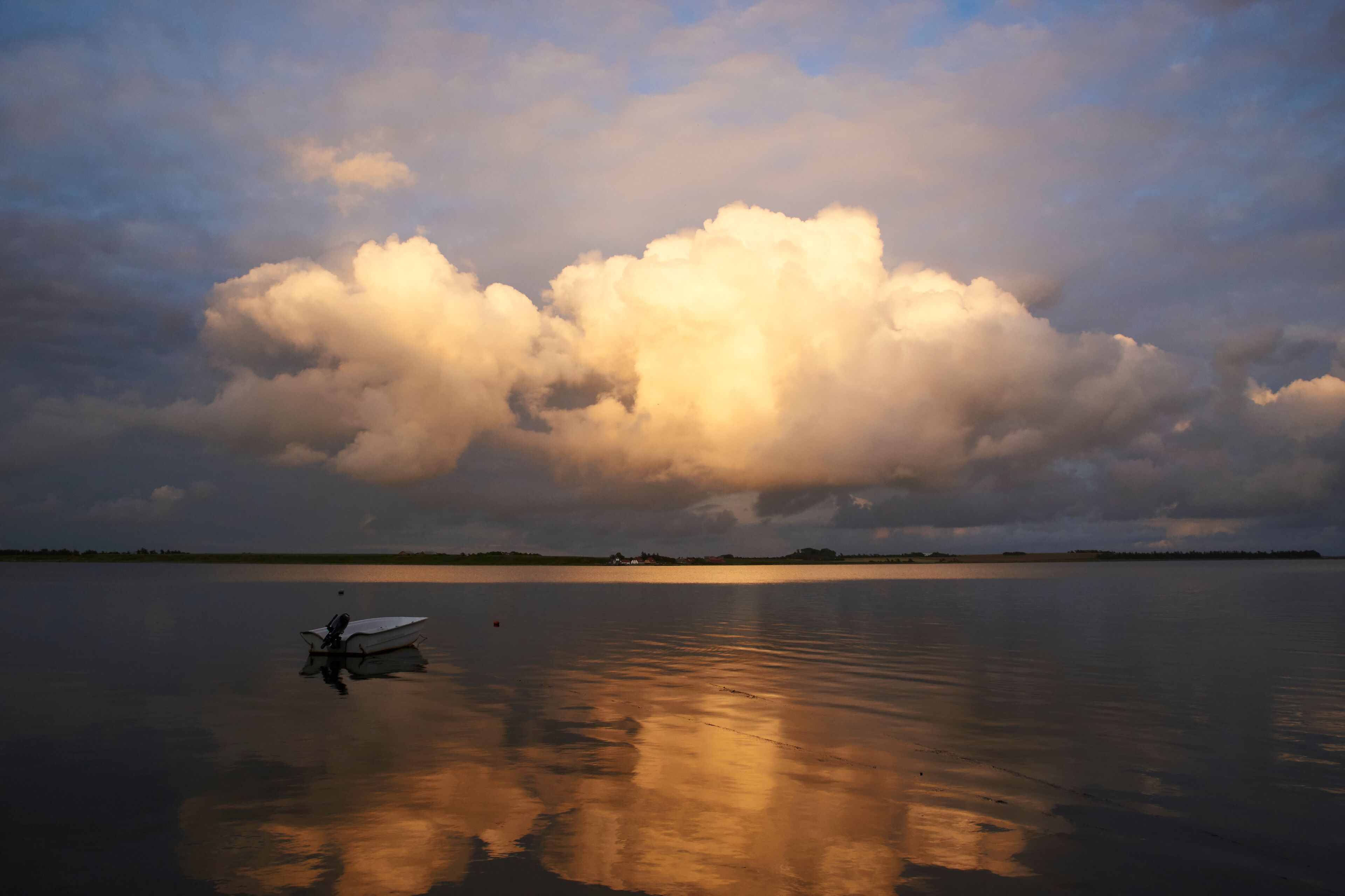 A calm lake with a large cloud formation and a small boat in the foreground.