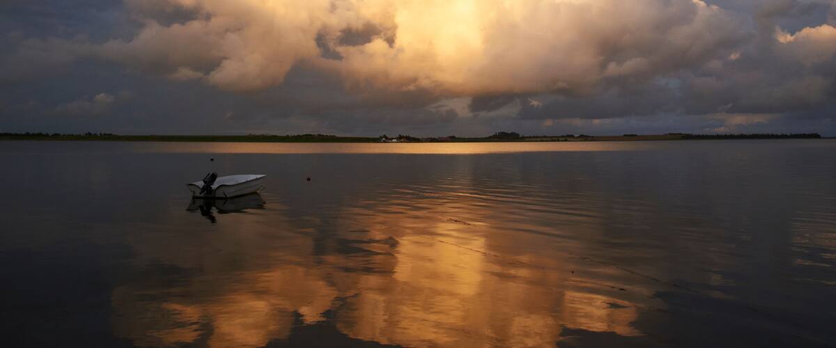 A calm lake with a large cloud formation and a small boat in the foreground.