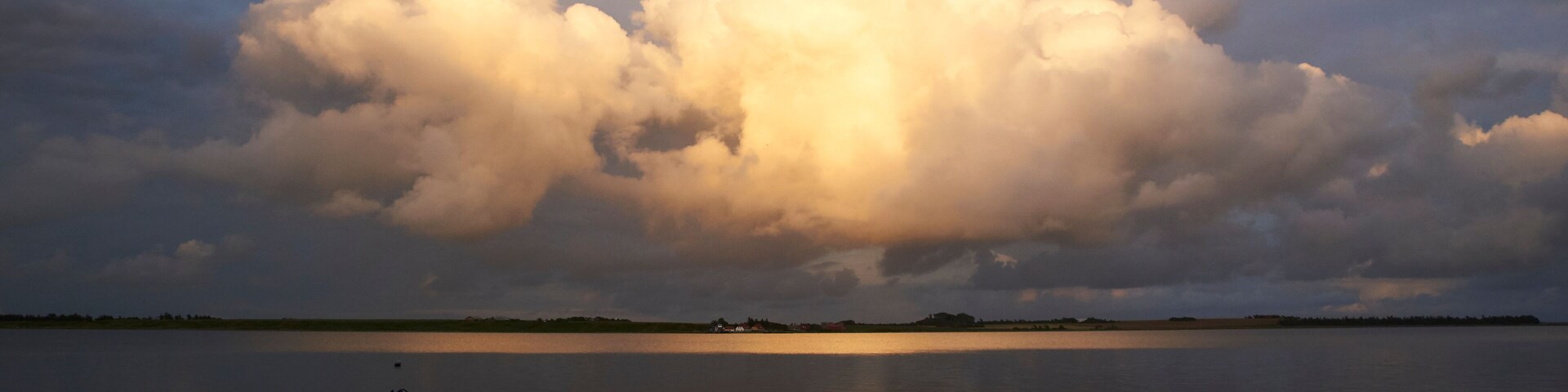 A calm lake with a large cloud formation and a small boat in the foreground.