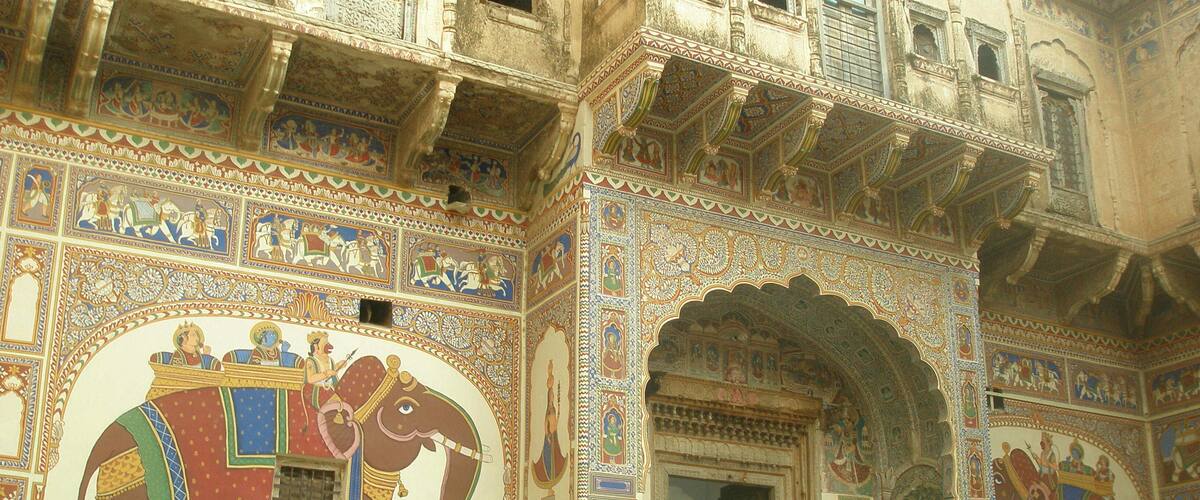 A building with intricate murals of elephants and figures, detailed architectural designs, and a large arched doorway.