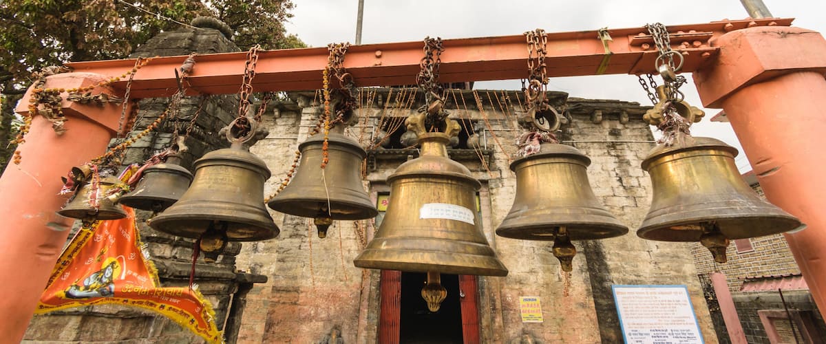A temple entrance with multiple large bells hanging from a red structure.