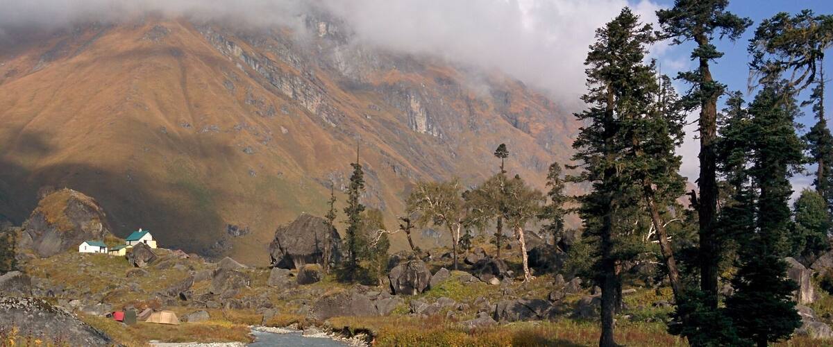 A river flowing through a mountainous landscape with a small settlement and tall trees.