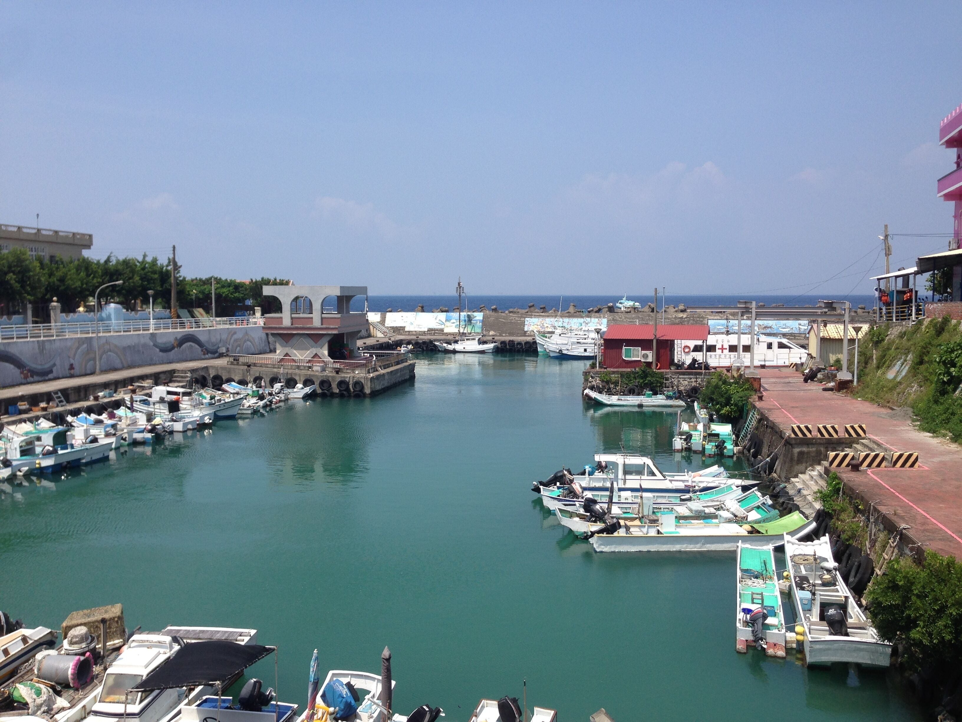 A marina with various boats docked, a pier, and buildings along the waterfront.