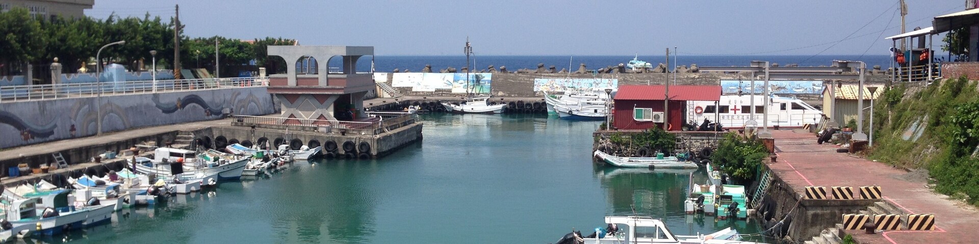 A marina with various boats docked, a pier, and buildings along the waterfront.