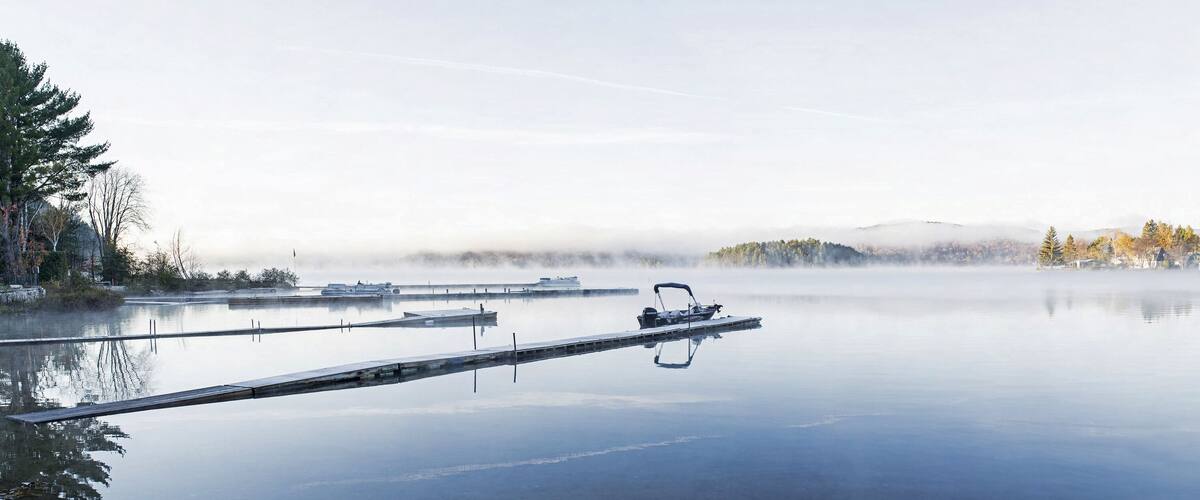 A calm lake with a dock and a boat, surrounded by autumn trees and mist-covered hills.