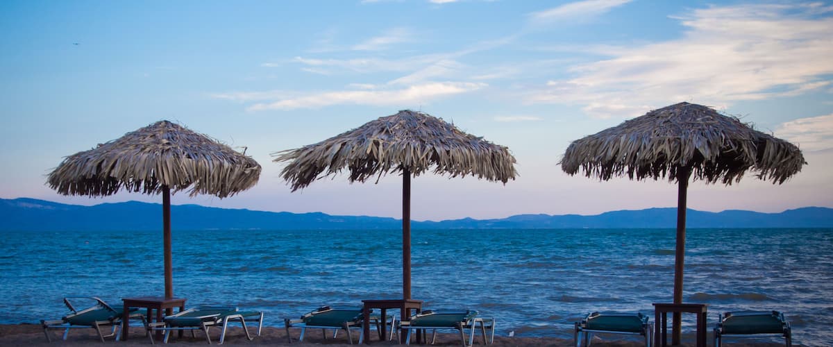 A beach with thatched umbrellas and lounge chairs.