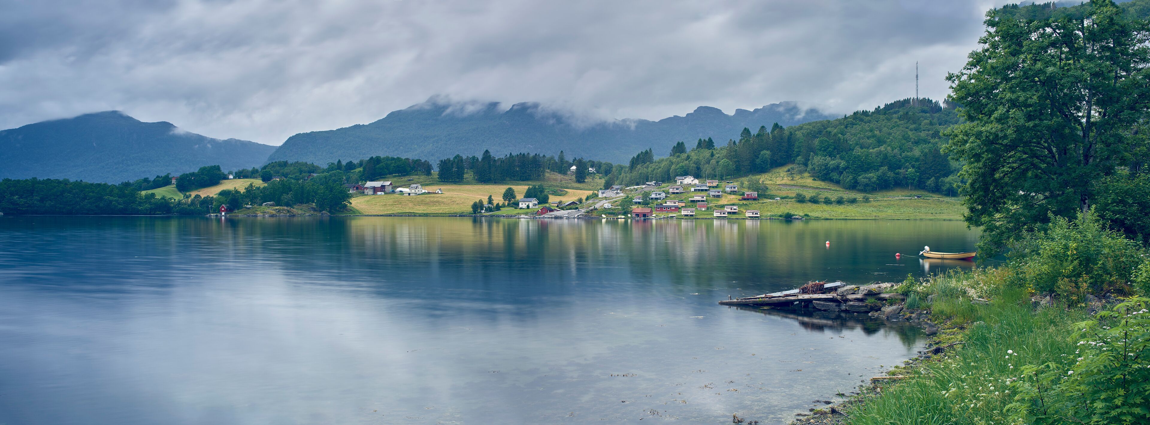 A calm lake with a small village and mountains in the background.