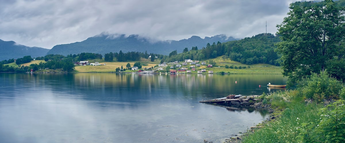 A calm lake with a small village and mountains in the background.