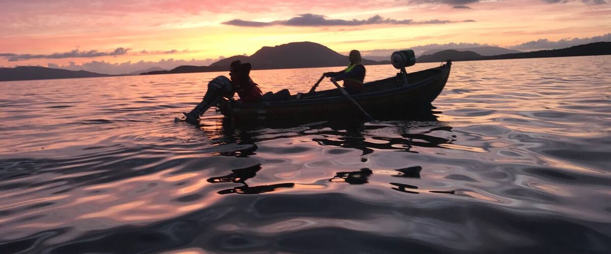 A sunset over a calm lake with a boat and two people rowing.