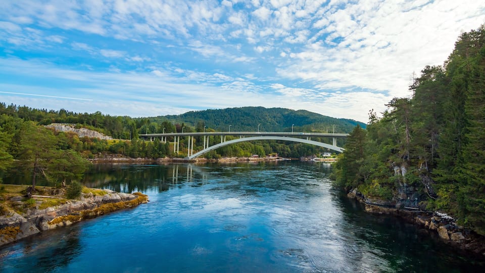 A river with a white bridge, surrounded by greenery and hills.