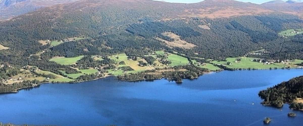 A lake surrounded by green fields and forested hills.