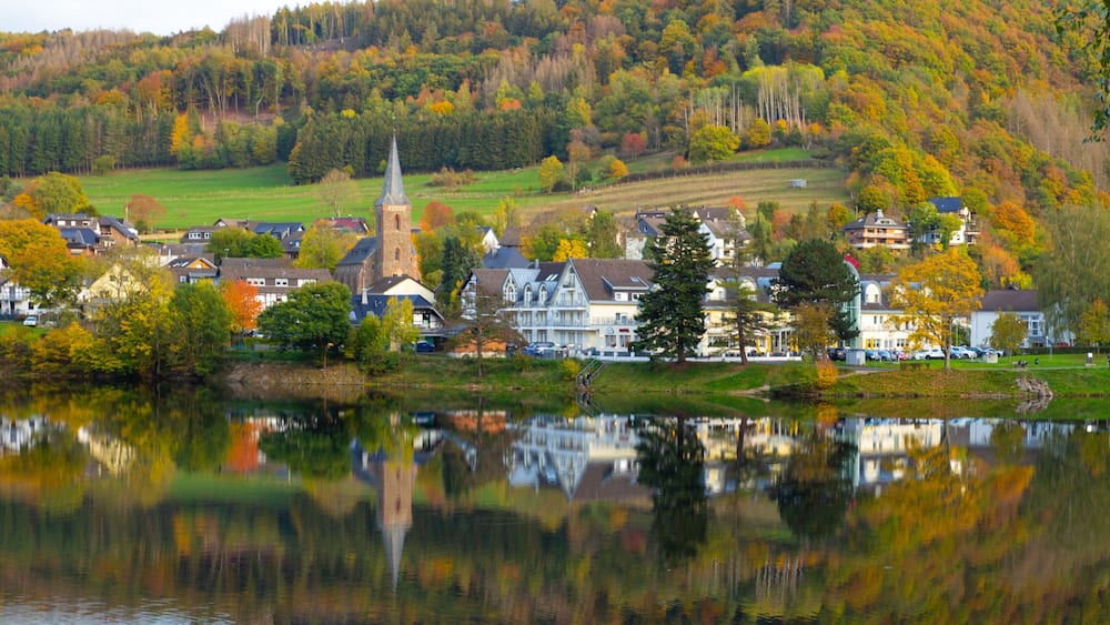 A lakeside town with a church steeple, houses, and autumn-colored trees.