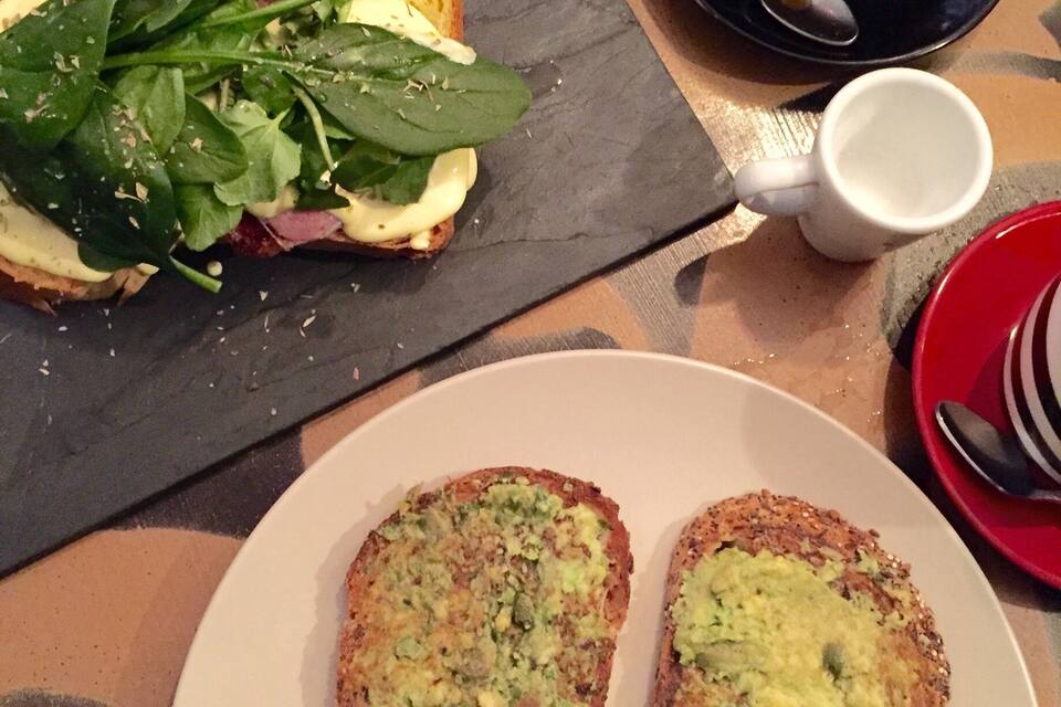 Un piatto di pane tostato con crema verde, una tazza di caffè e un piatto di verdure su un tavolo.