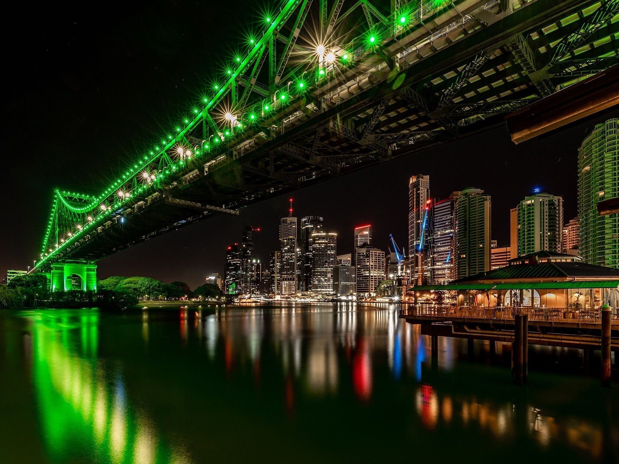 Un paisaje urbano nocturno con un puente iluminado que se refleja en el agua.