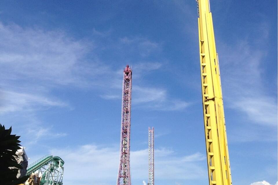 A theme park with a tall yellow tower, a pink roller coaster, and a green roller coaster.