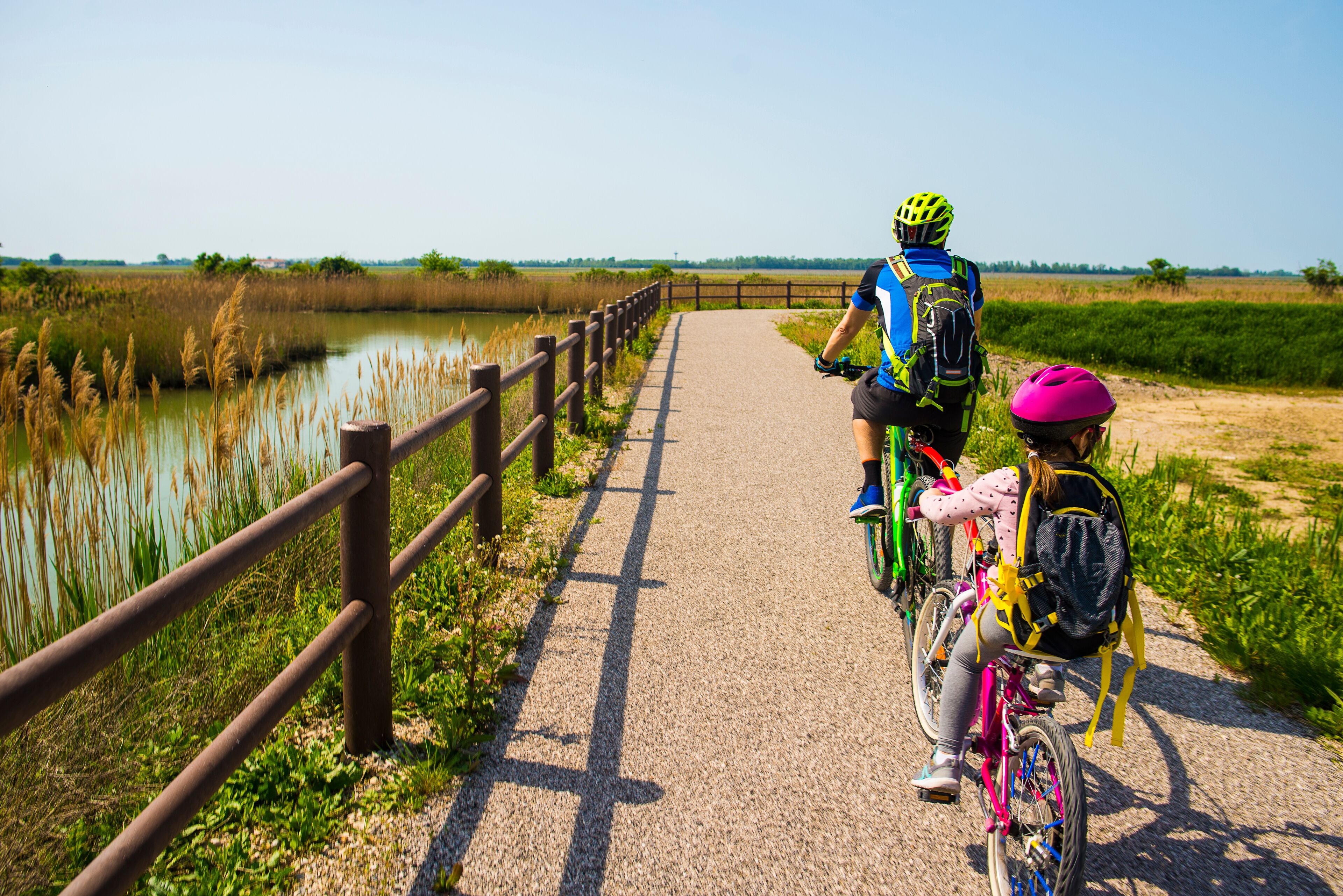 Father and daughter tandem going in bicycle. The bike itinerary FVG2 of Grado city, Friuli Venezia Giulia, region of Italy. Family, education, recreation and sport concept.