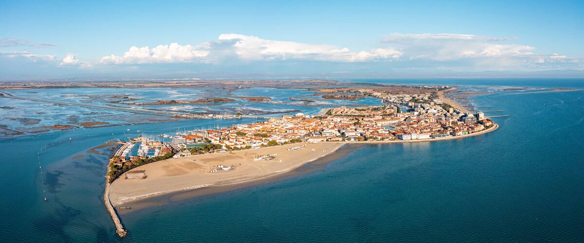 An aerial view of a coastal town with a beach, marina, and surrounding water bodies.