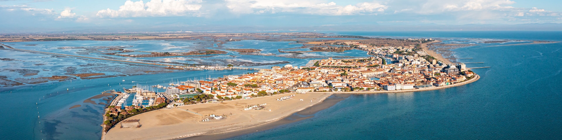 An aerial view of a coastal town with a beach, marina, and surrounding water bodies.