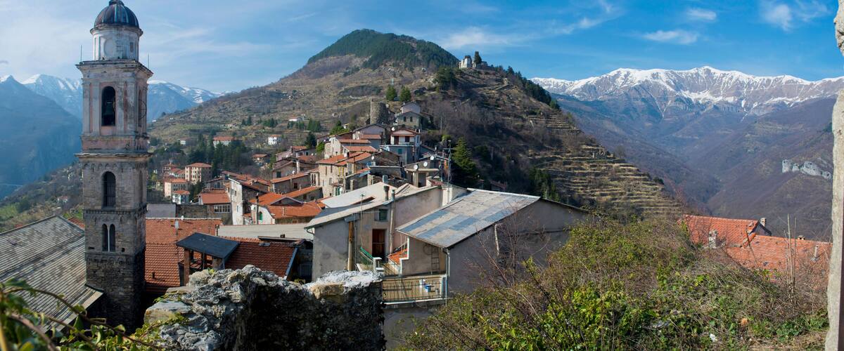 A mountainous village with a prominent church tower, terraced fields, and snow-capped peaks in the background.