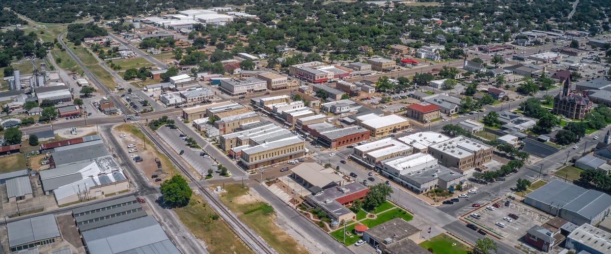 An aerial view of a town with industrial buildings, roads, and surrounding greenery.