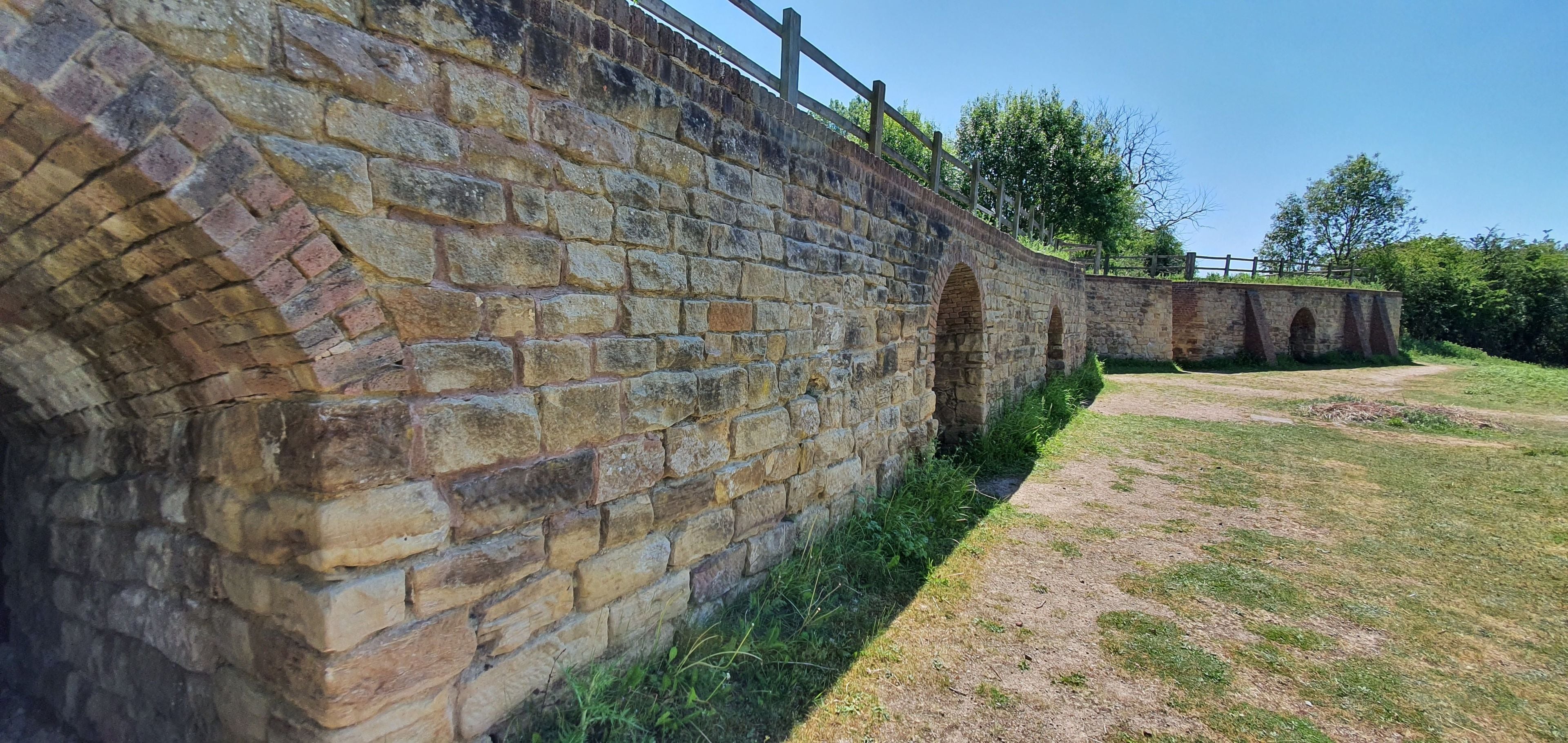 Mur de pedra amb una tanca de fusta i un pont arcat.