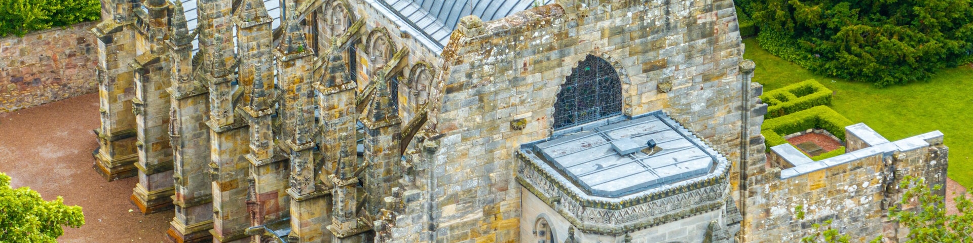 An old stone building with a large glass roof, surrounded by lush greenery.