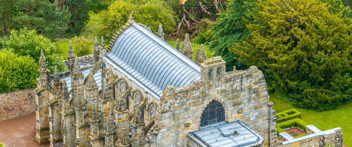 An old stone building with a large glass roof, surrounded by lush greenery.