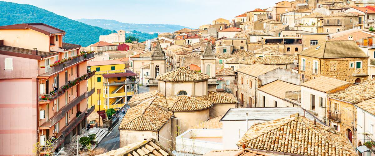 A densely packed urban area with terracotta-tiled rooftops, colorful buildings, and a mountainous backdrop.