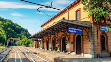 A train station with a covered platform, tracks, and a building with arched windows.