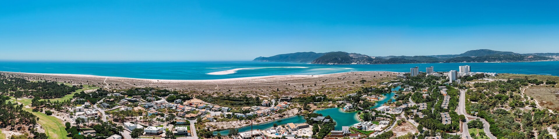 A coastal town with a beach, turquoise waters, and a mix of residential and commercial buildings.