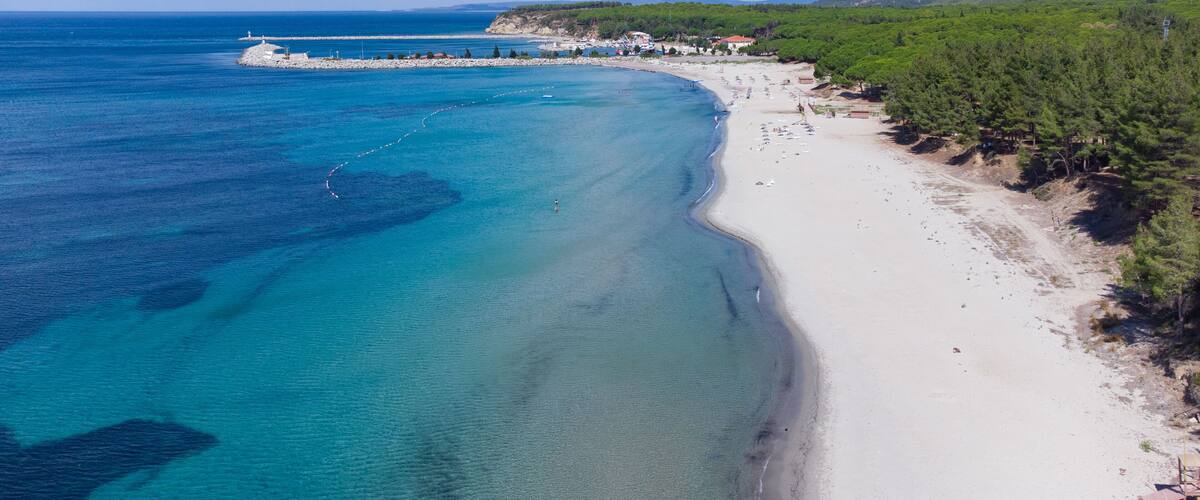 A coastal beach with clear turquoise waters, a sandy shore, and a forested hillside.
