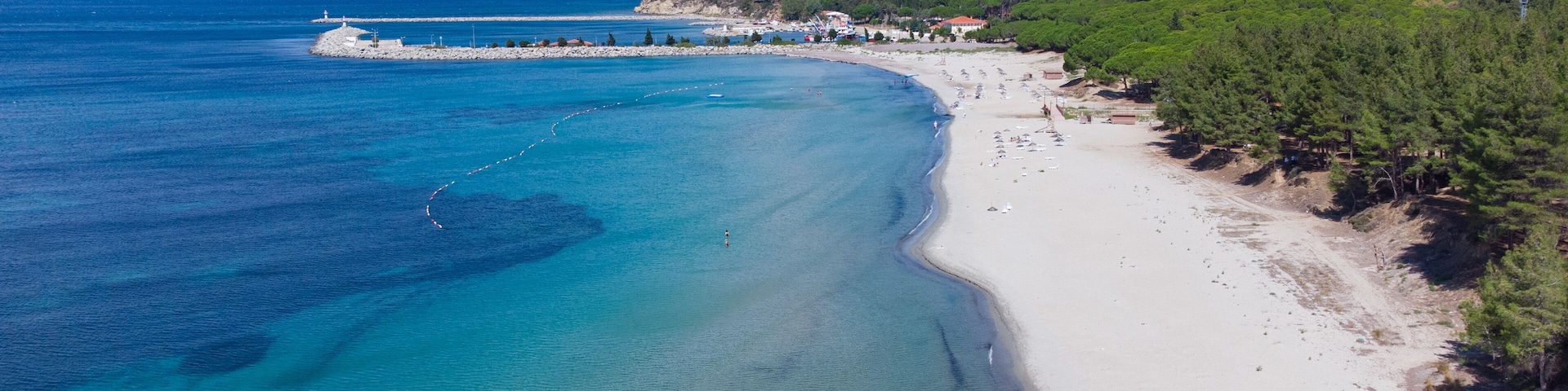 A coastal beach with clear turquoise waters, a sandy shore, and a forested hillside.